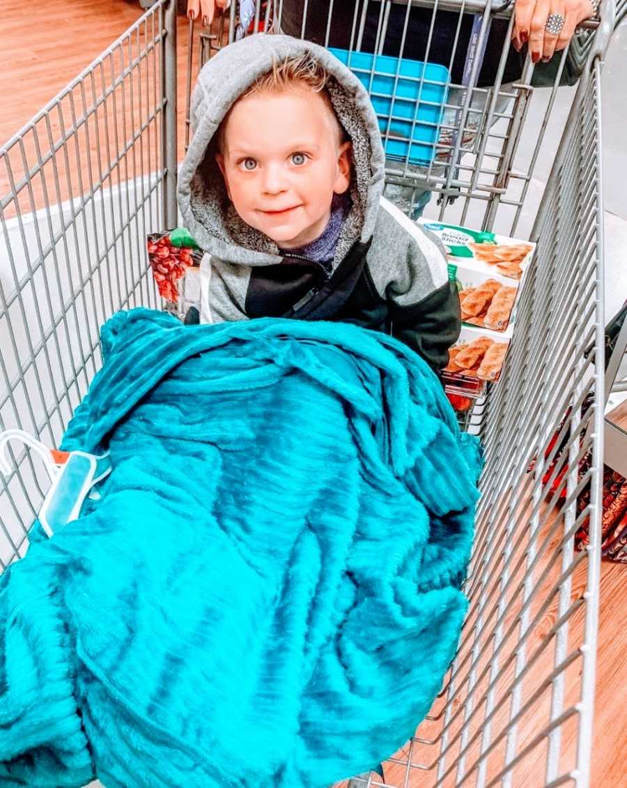 A little boy sits in a blanket in a shopping cart