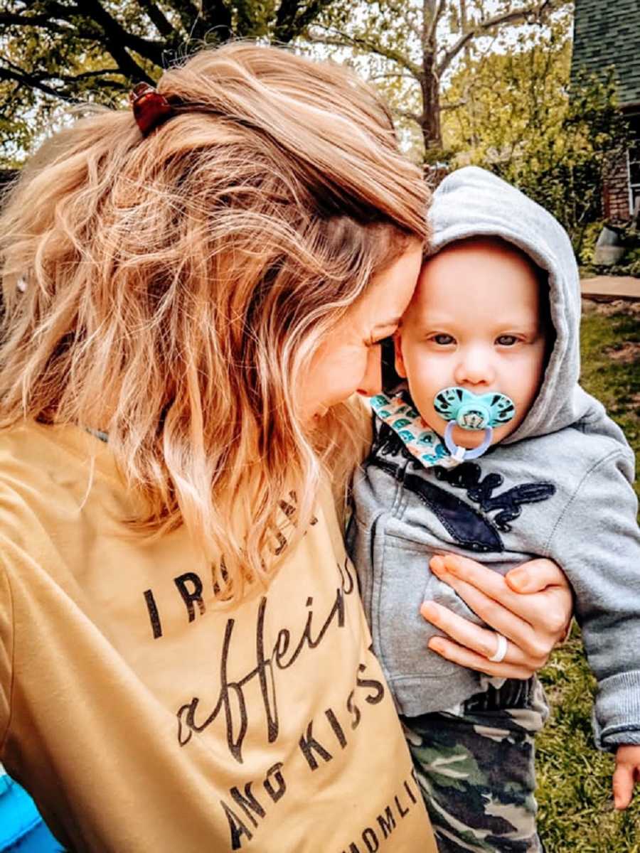 A mother holds her toddler, who has a pacifier in his mouth