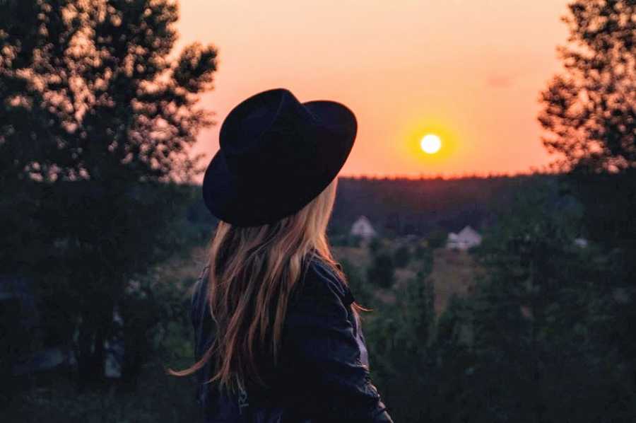 A woman in a hat looks at a sunset