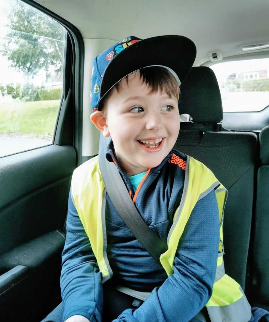 Boy sitting in car wearing hat and vest