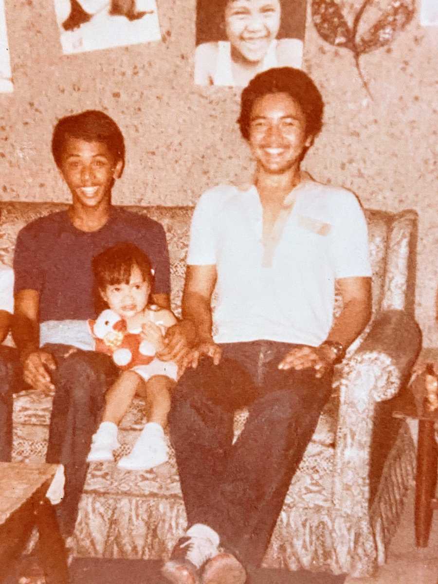 A girl sits on a couch with two of her brothers