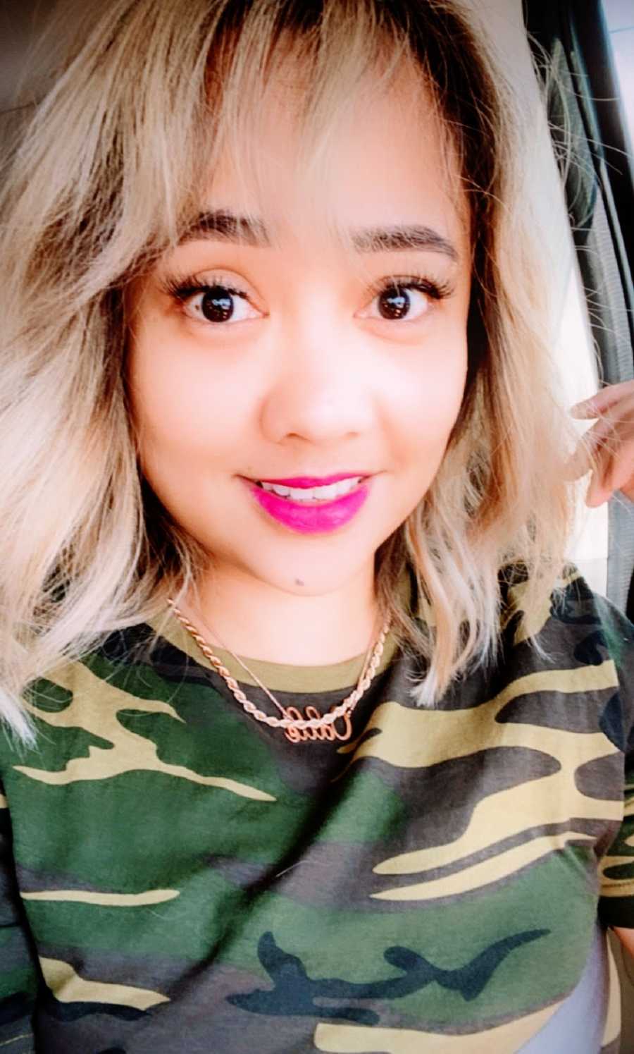 A woman wearing a camouflage shirt sits in her car