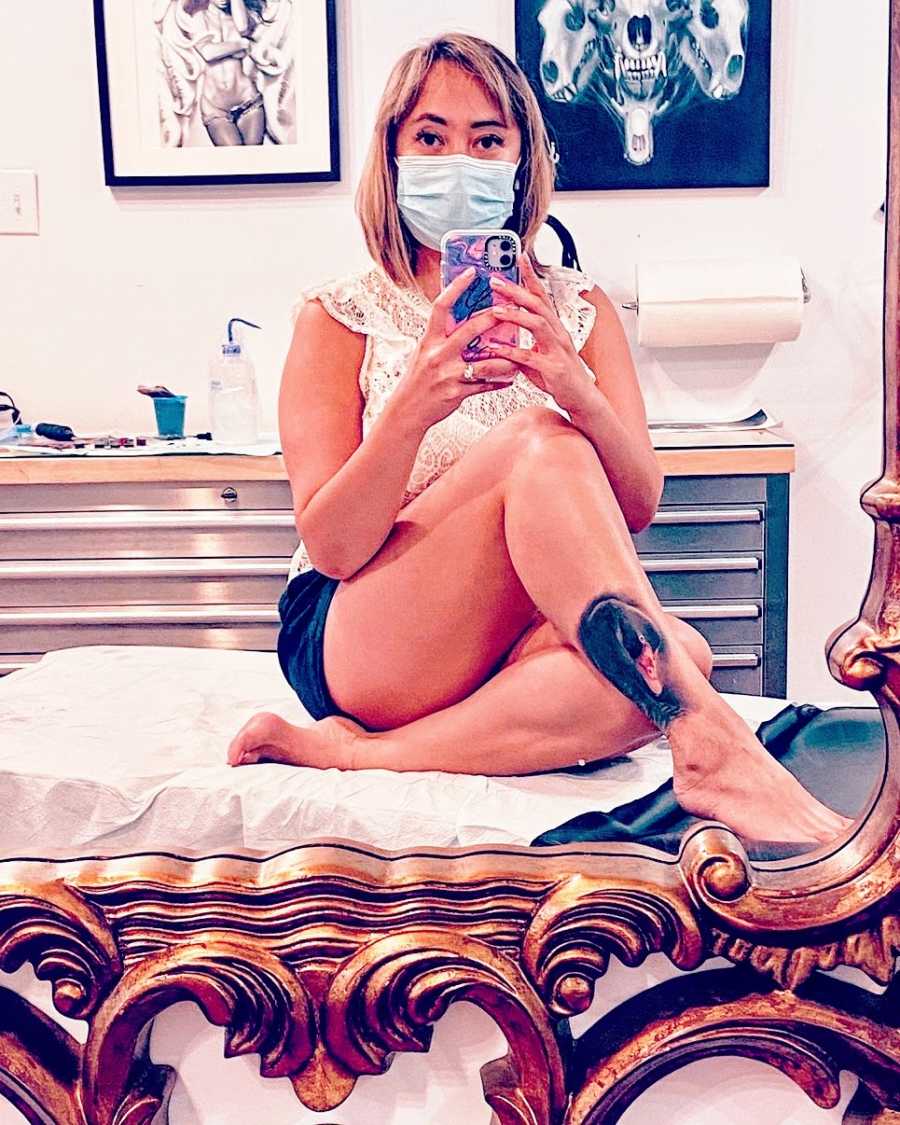 A woman sits on a bed wearing a mask with her legs crossed