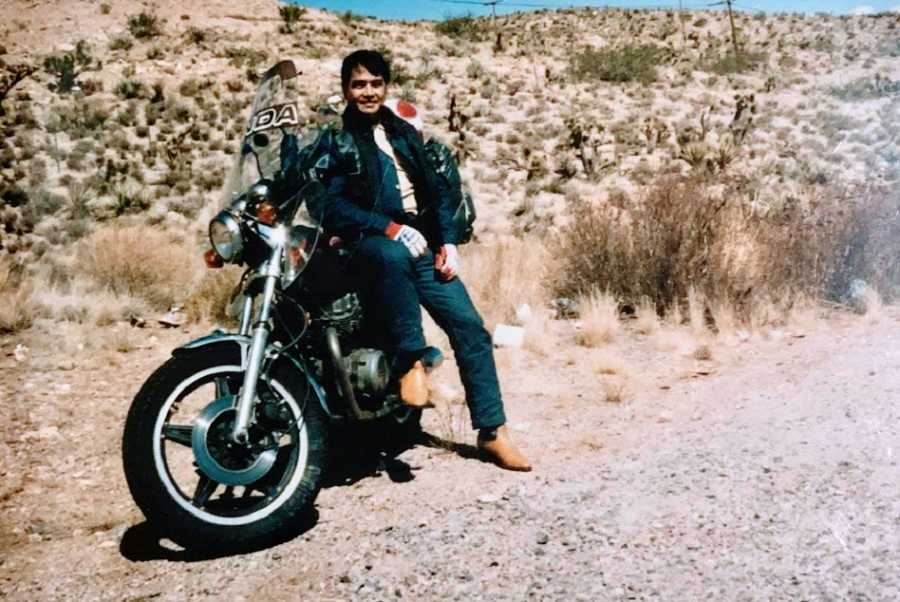 A man sits by a motorcycle out in the desert