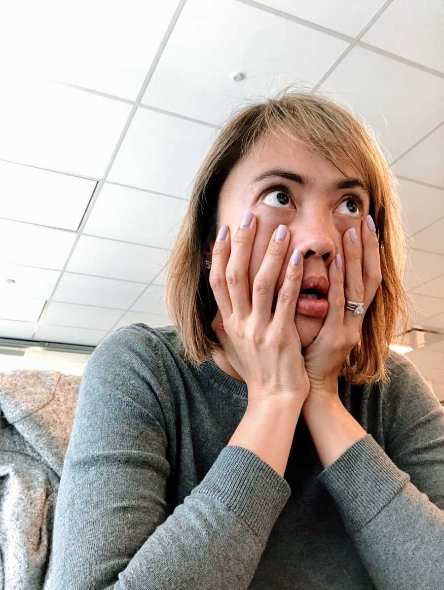 A woman holds her face between her hands with surprised eyes