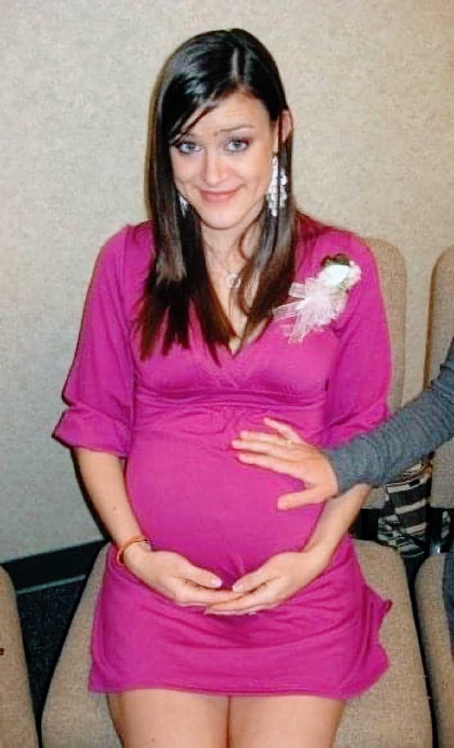 Pregnant young mom in pink dress holds belly