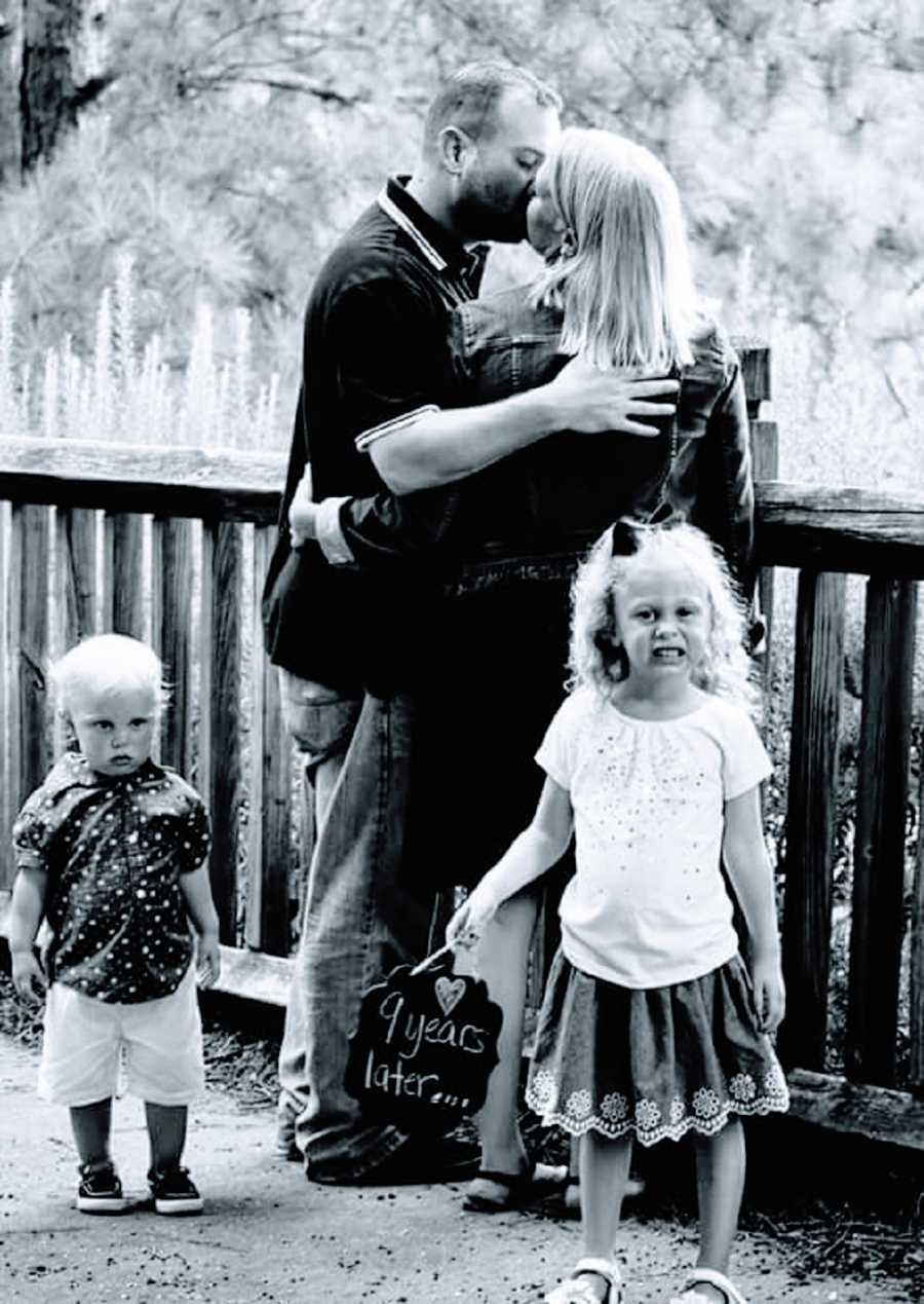 A husband and wife kiss while their two children stand nearby