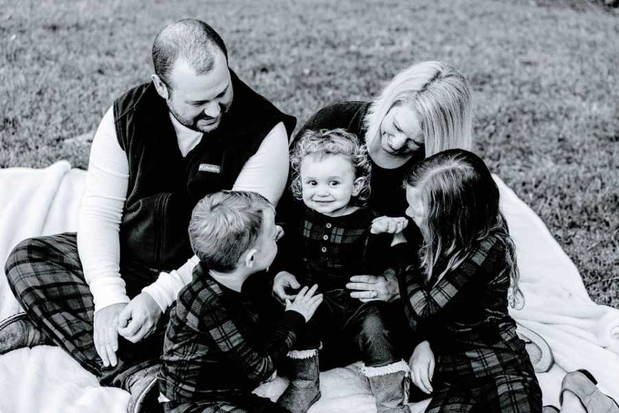 A husband and wife sit with their three young children