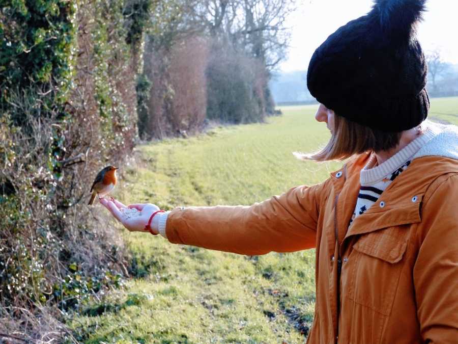 Woman holds out her hand where a bird sits