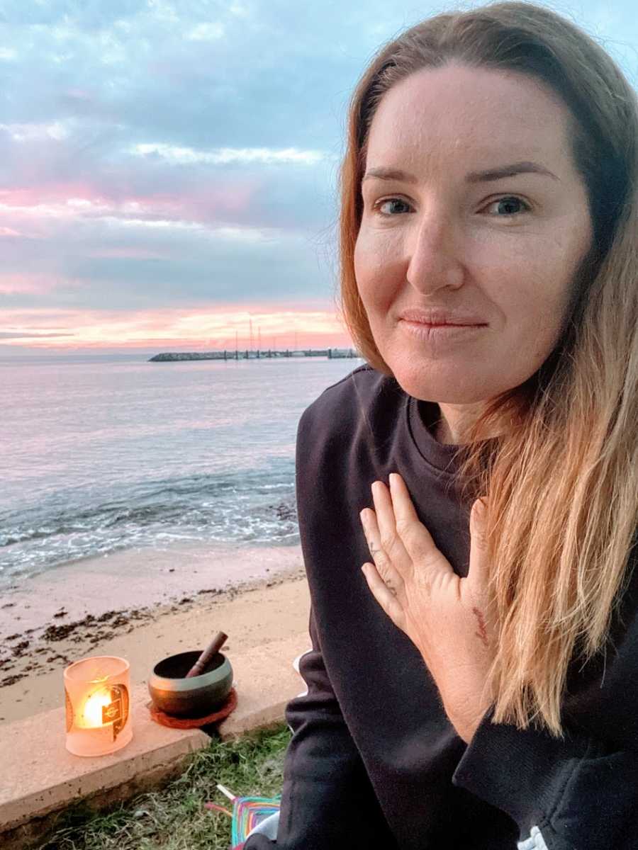 A woman stands at the beach with one hand over her heart