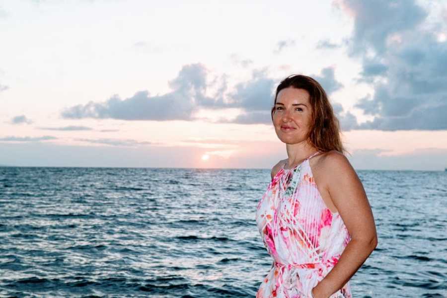 A mother wearing a pink dress stands by the water