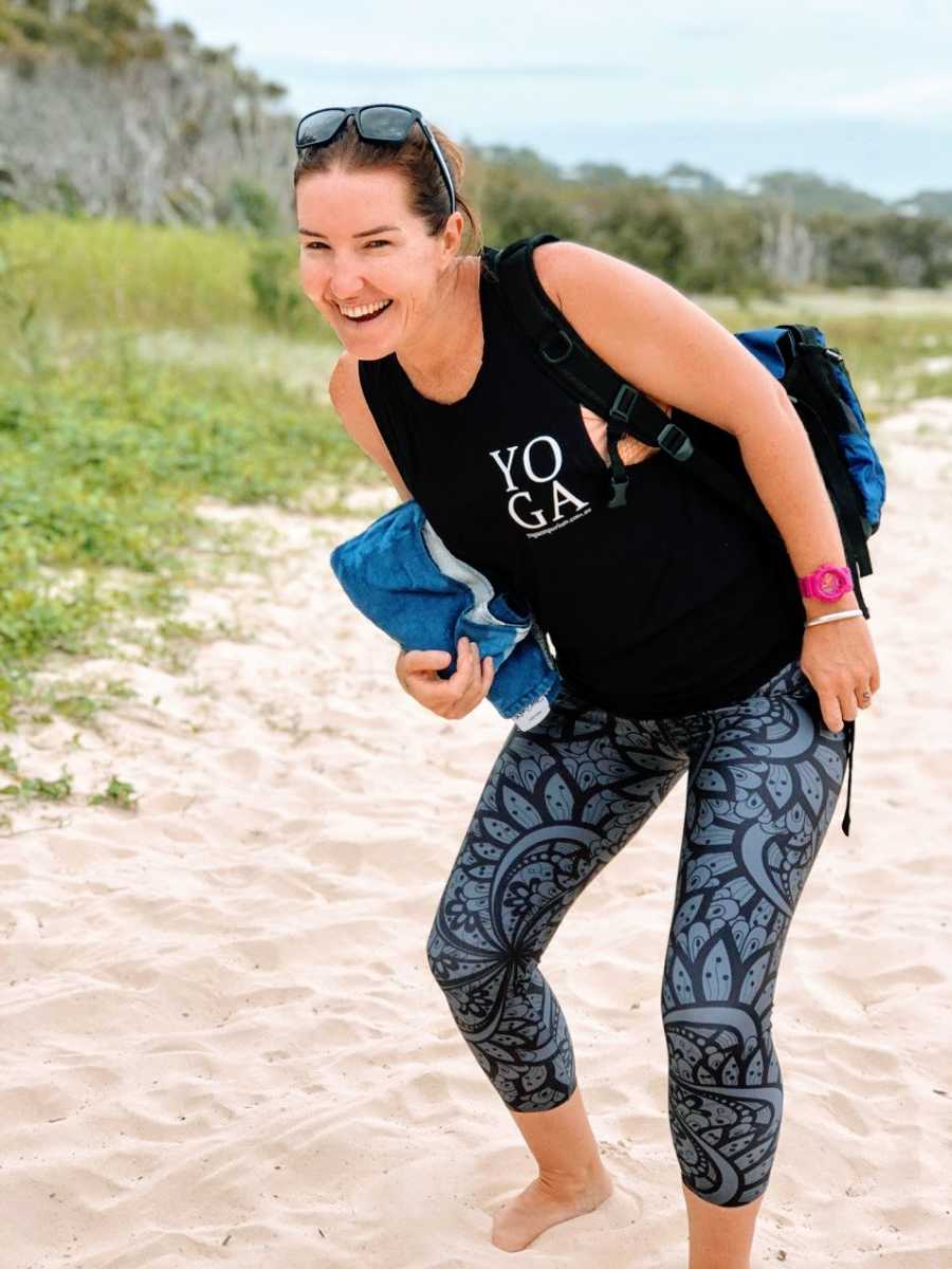 A mother stands in the sand wearing a yoga outfit
