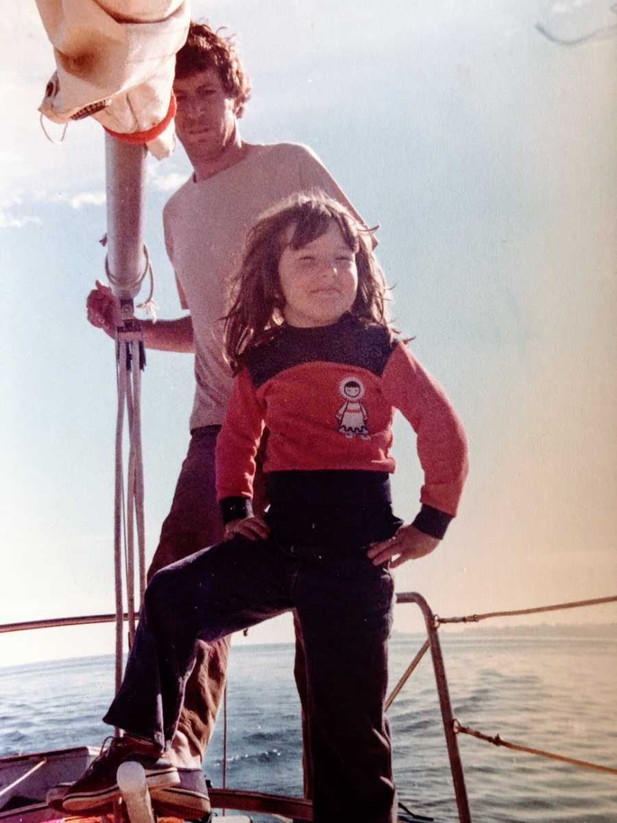 A little girl stands on a boat with her hands on her hips