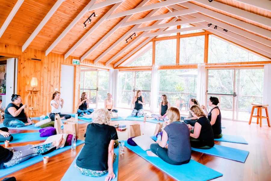 A woman sits with a class full of people on yoga mats