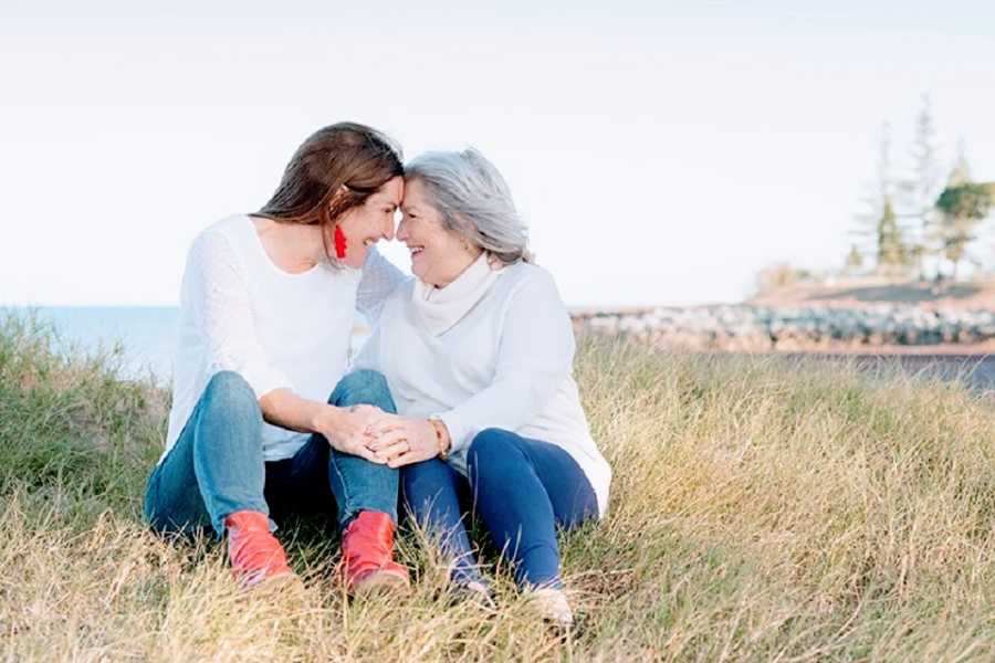 A woman and her mother sit together in a grassy field