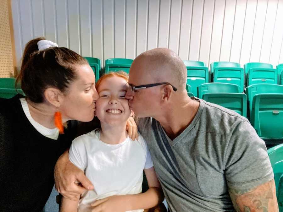 Parents kiss their daughter on either cheek