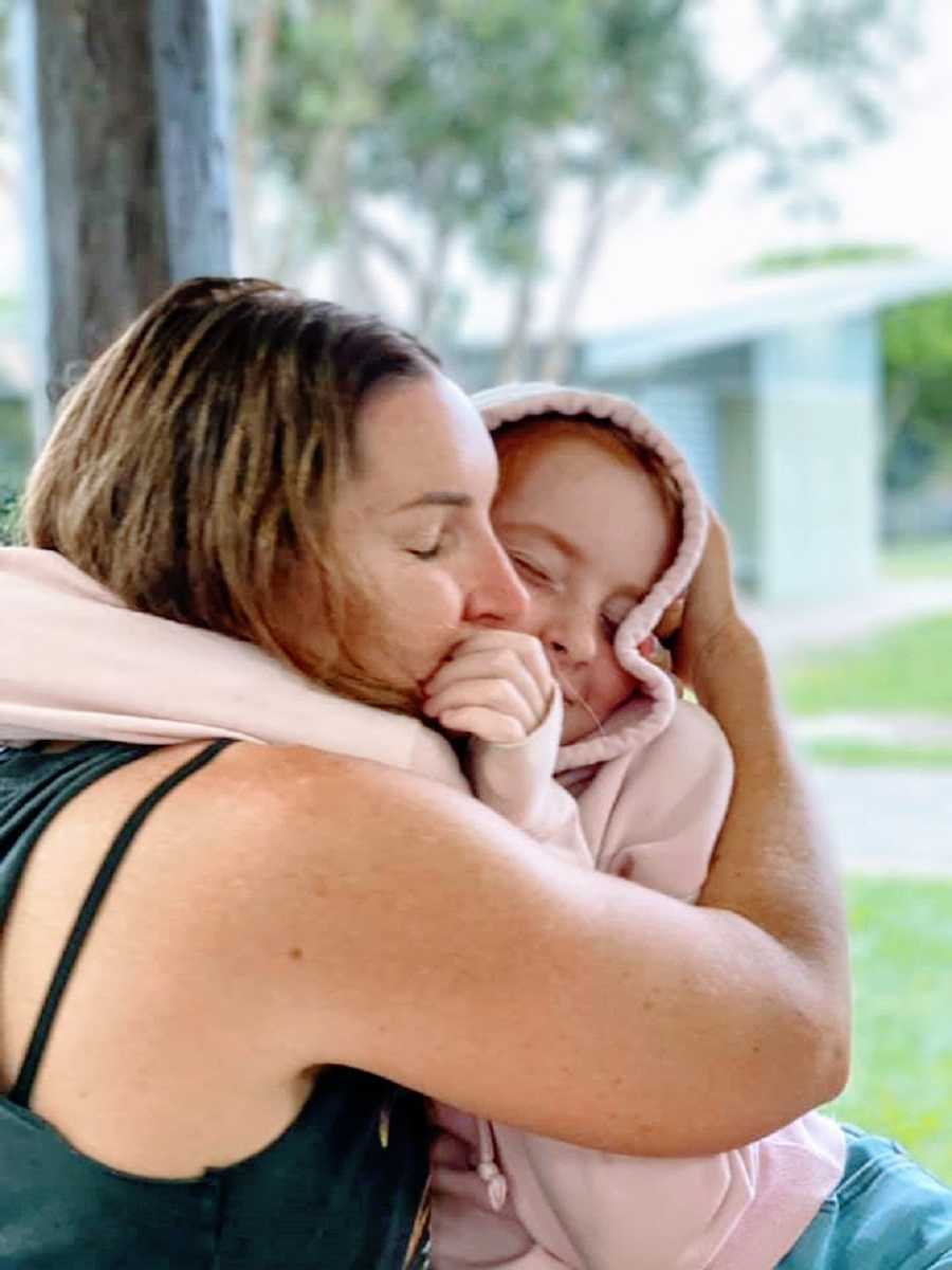 A mother hugs her daughter who is wearing a pink hoodie