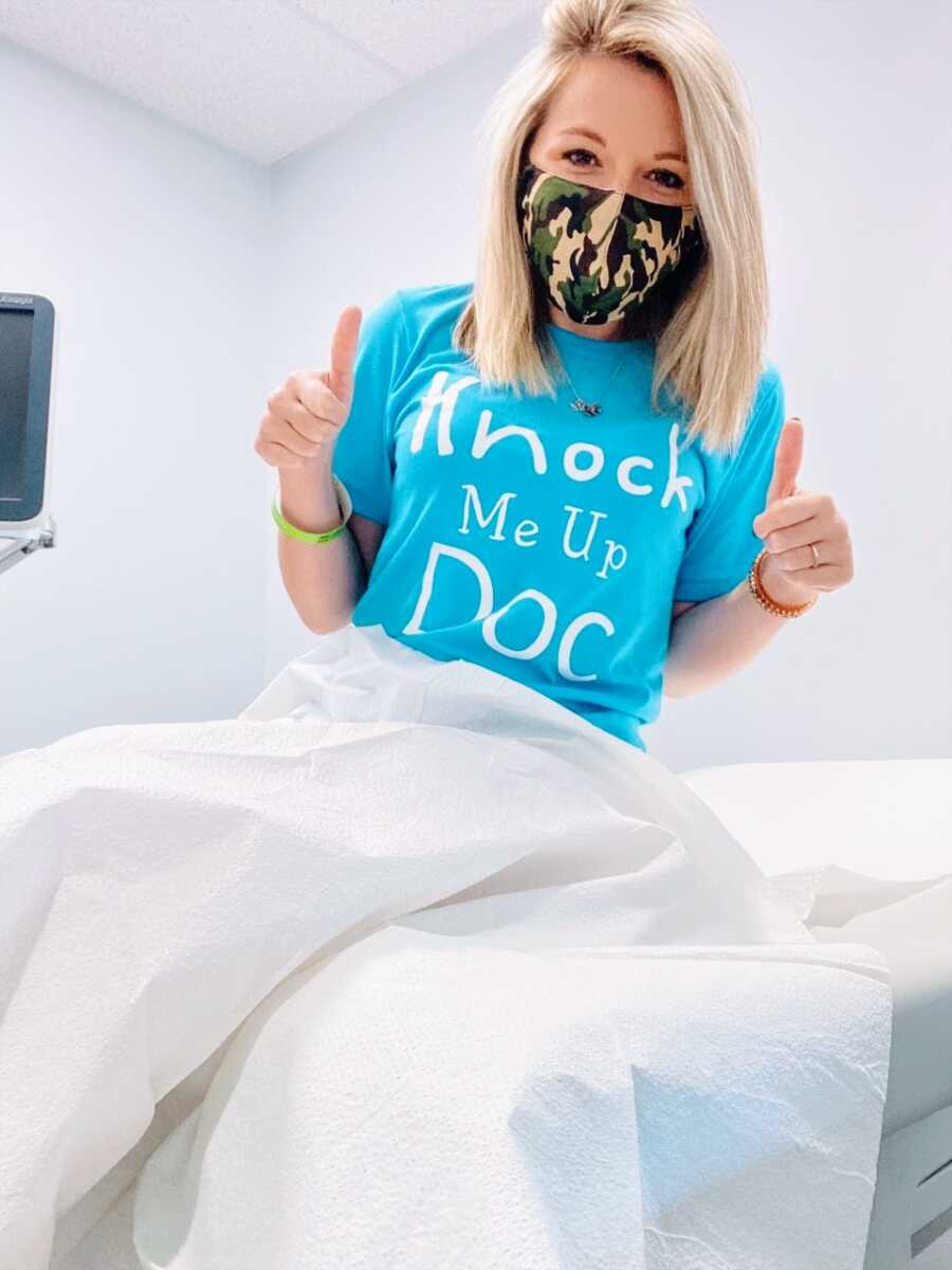 Woman struggling with infertility takes a selfie before getting an IUI while wearing a blue shirt with the words "Knock me up Doc" on it