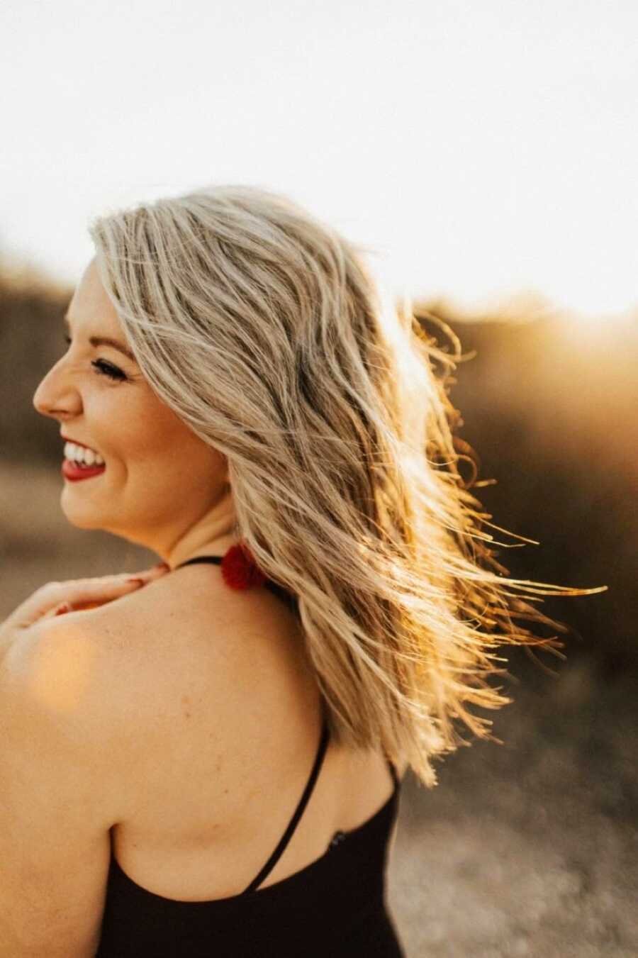 Woman struggling with unexplained infertility smiles for a photo while her wavy hair blows in the wind during golden hour