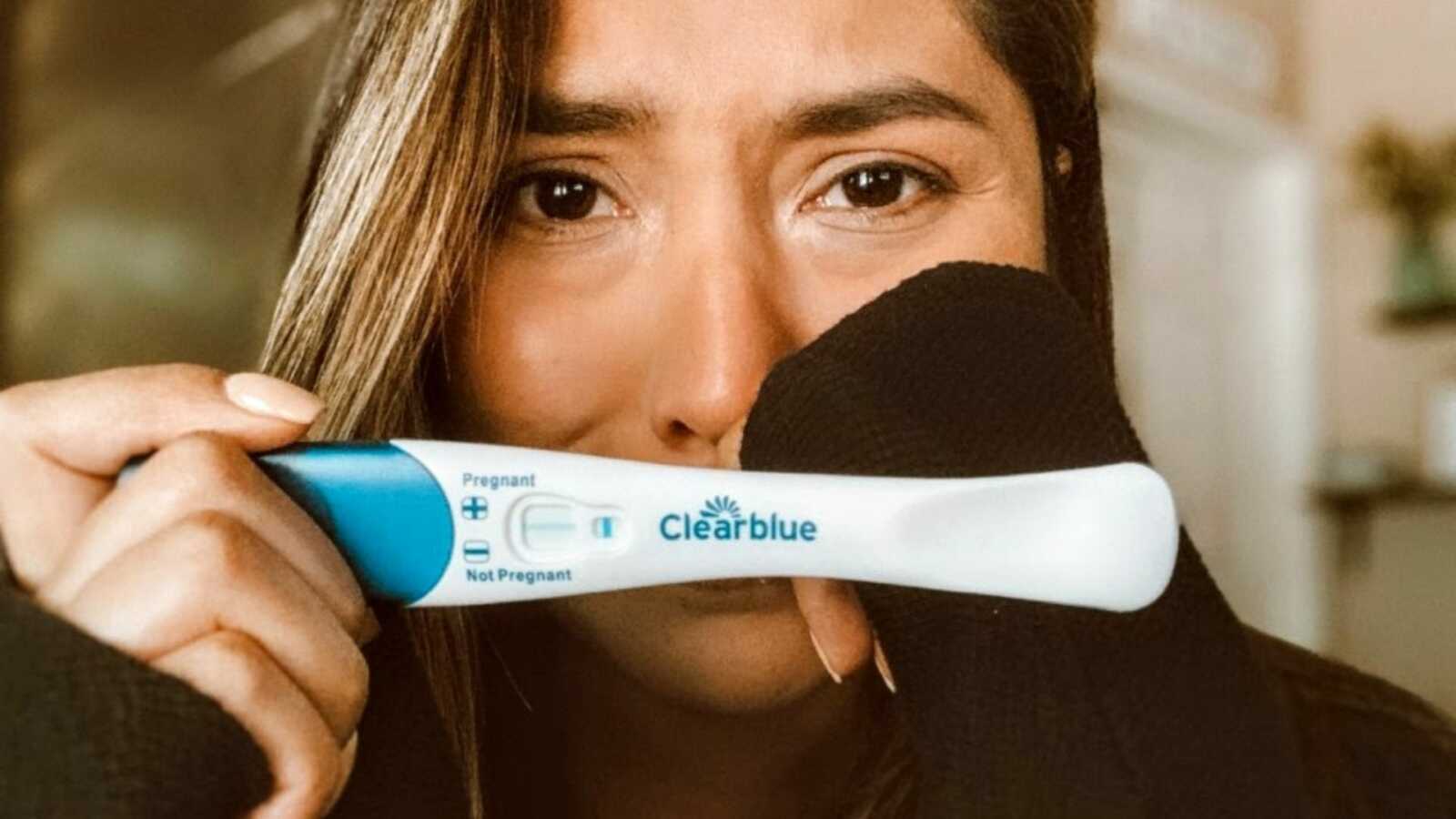 Woman holds up a negative pregnancy test while crying