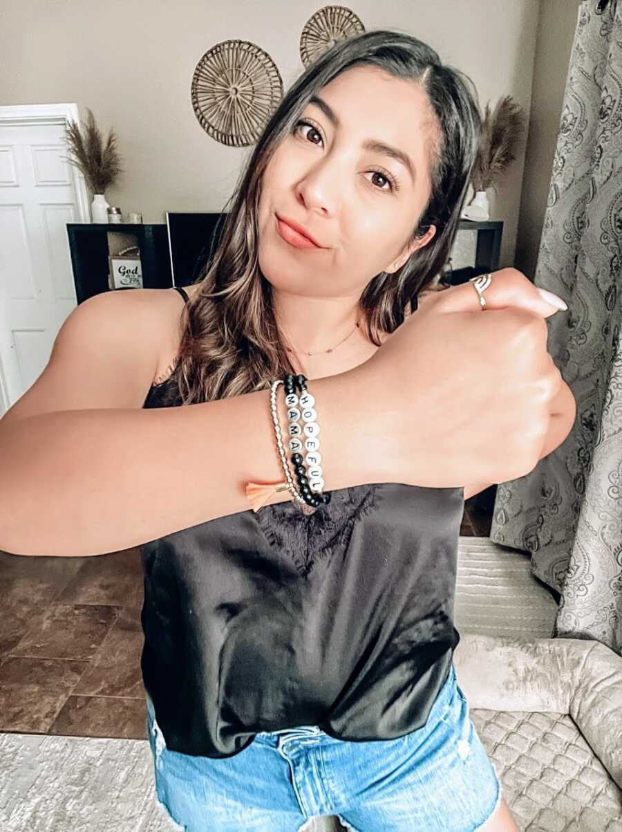 Woman trying to conceive and struggling with infertility takes a photo of herself wearing bracelets that says "hopeful mama"