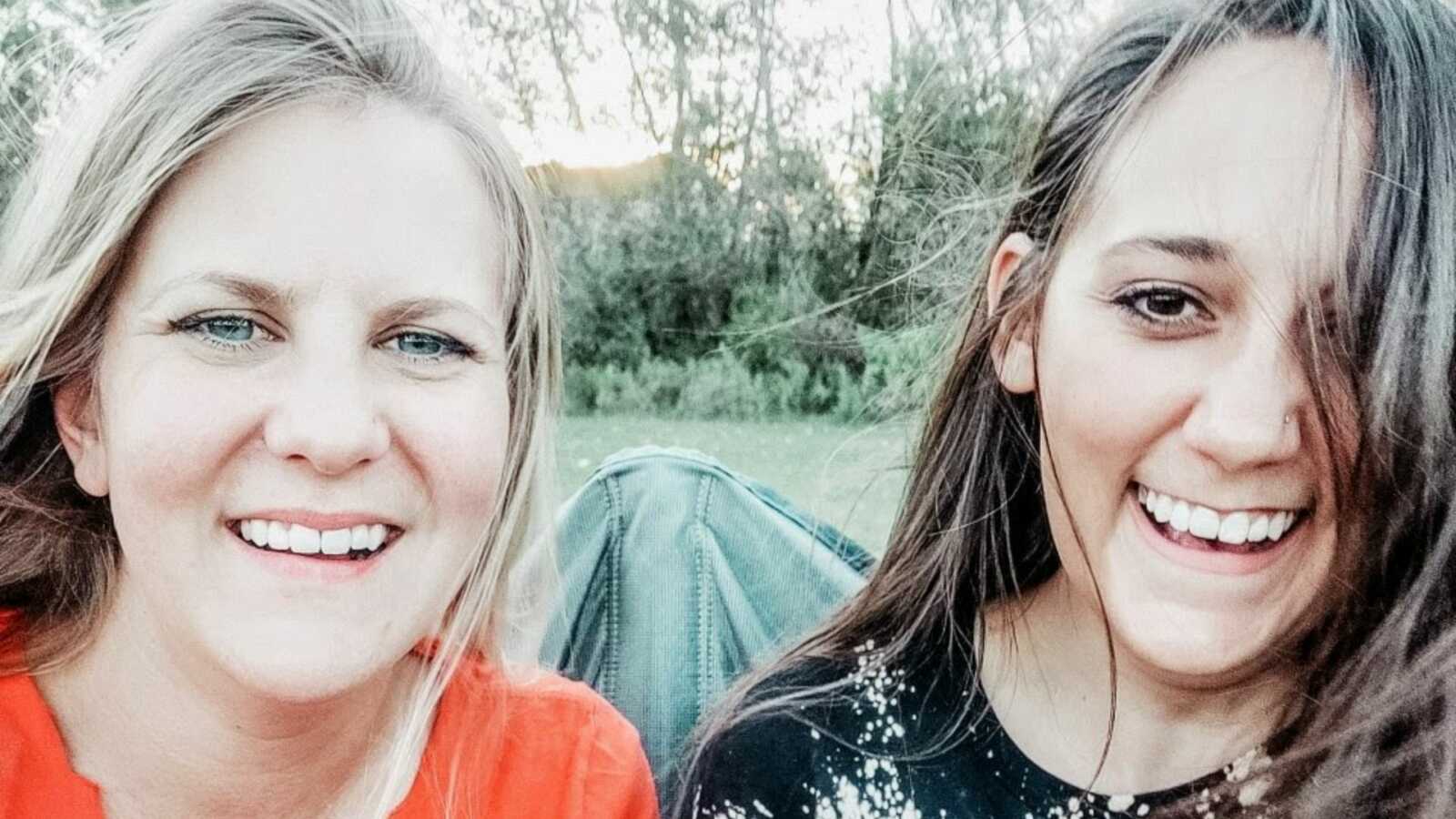 Mom and stepmom giggle together while taking selfies at one of their kids' football games