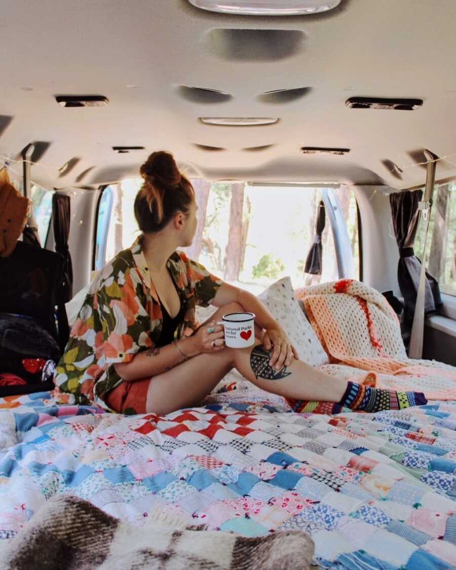 Woman looks out over the view out of the back of her van she travels in with her boyfriend