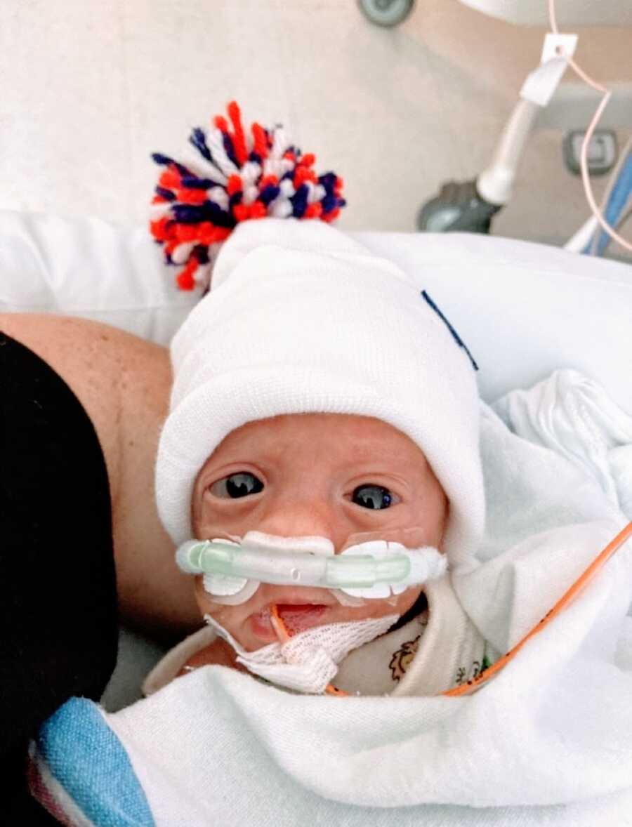 Mom snaps photo of one of her newborn preemie twins wearing a beanie with a red white and blue pompom on it