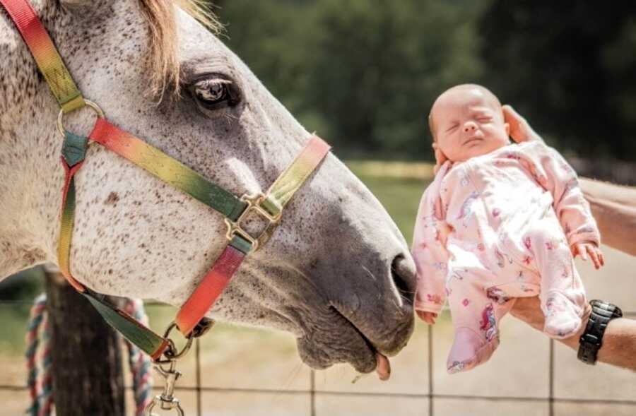 Mom holds one of her twin daughters up to a horse on her Kentucky farm