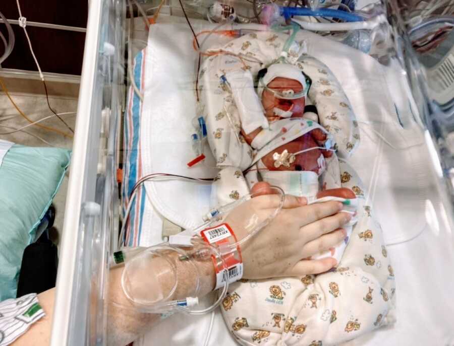 Mom snaps a photo of one of her twins laying in an isolette in the NICU 