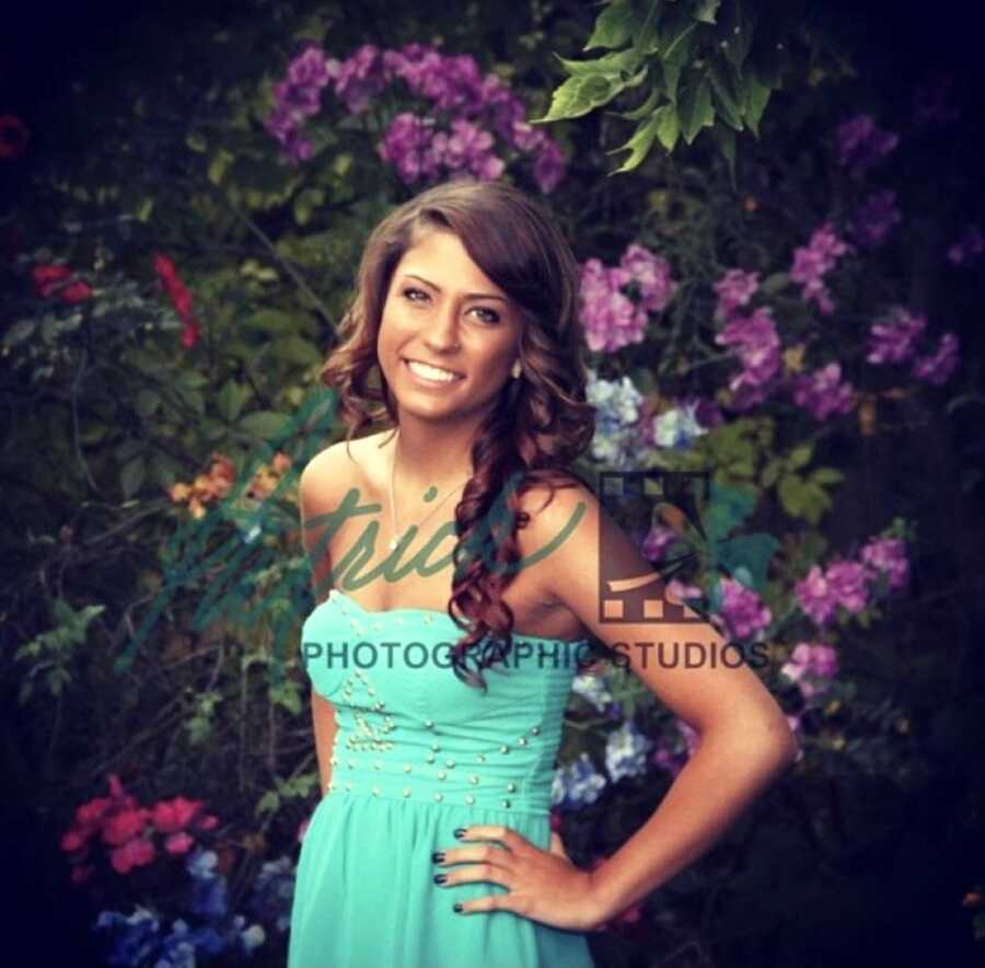 Teenage girl in emerald dress poses for photos in front of flowers before her homecoming dance