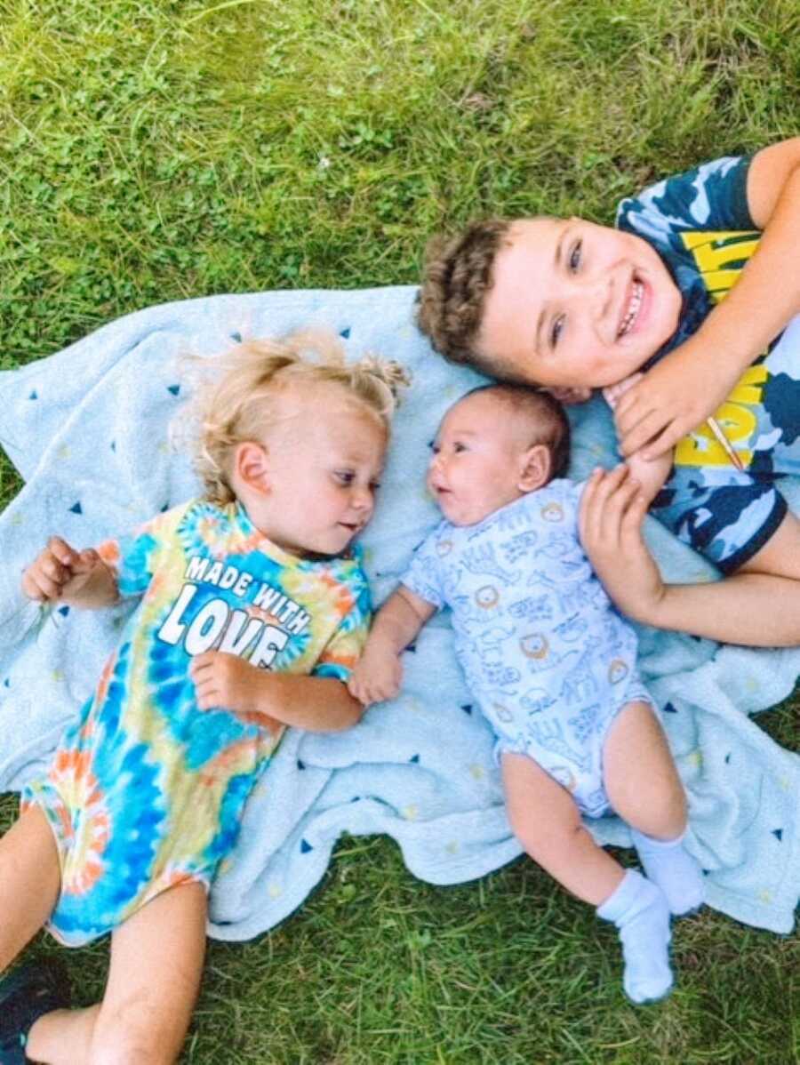 Boy mom takes a photo of her three sons laying together on a blanket outside
