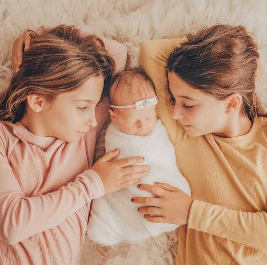 Twin daughters cuddle their newborn baby sister in newborn photoshoot