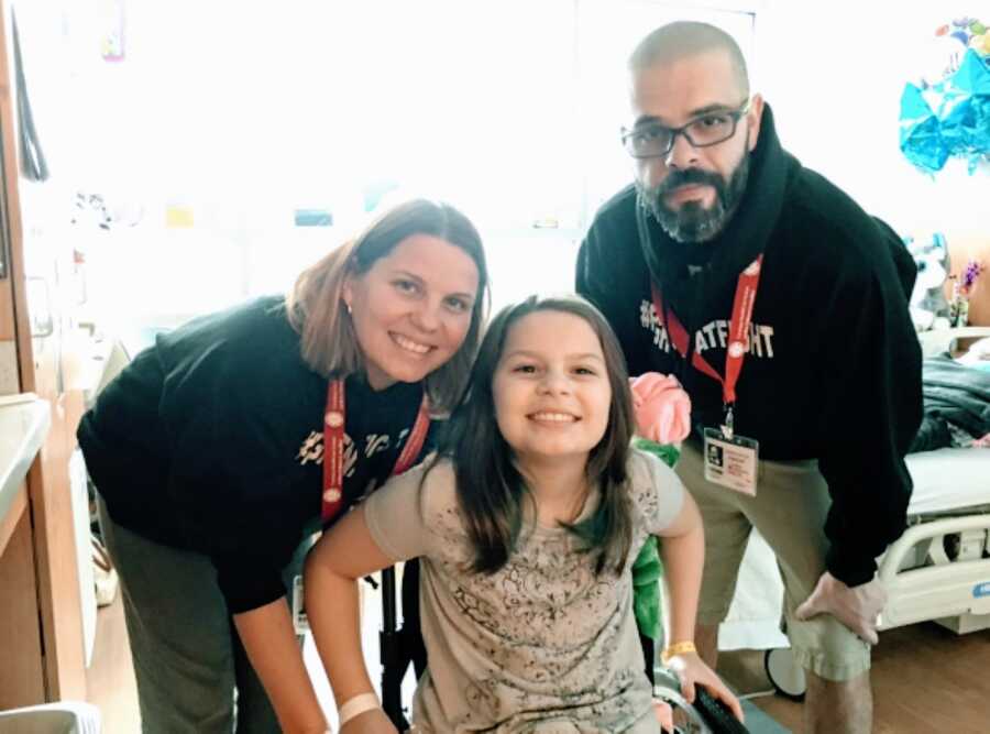 Parents take a photo with their daughter partially paralyzed due to a spinal stroke while wearing "FIGHTNATFIGHT sweatshirts