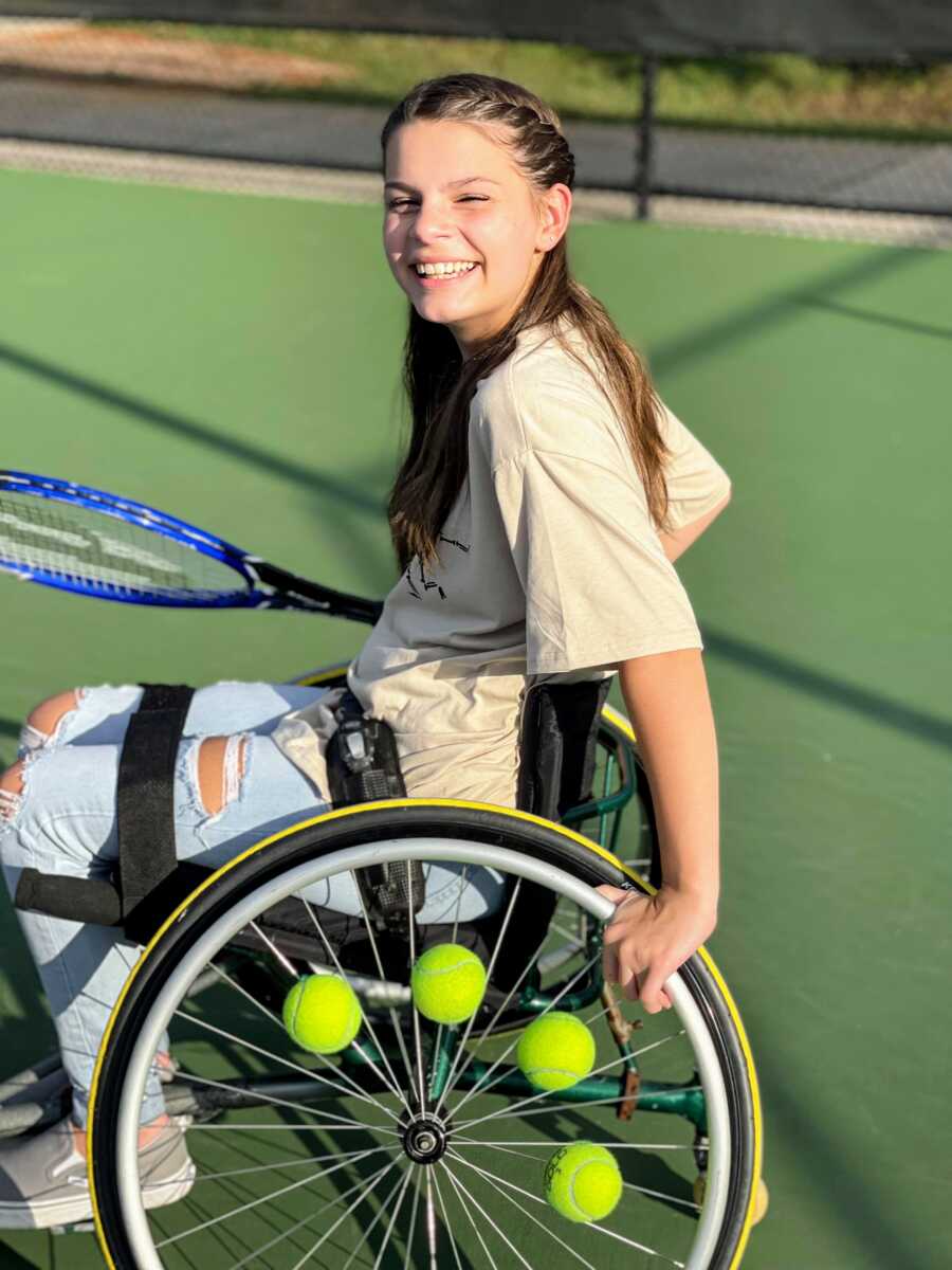 Young girl playing adaptive tennis smiles big while holding a tennis racket