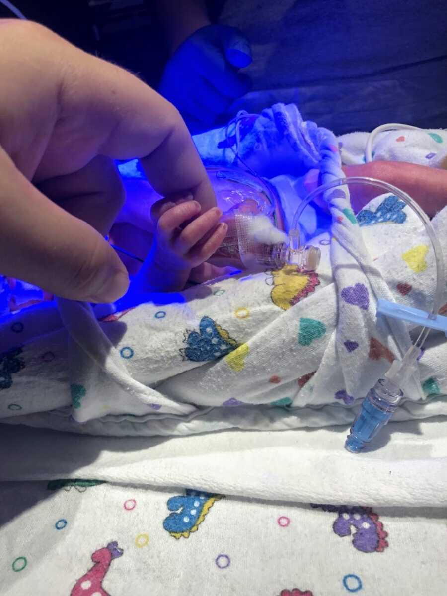 NICU mom lets her child hold her finger while intubated in an isolette