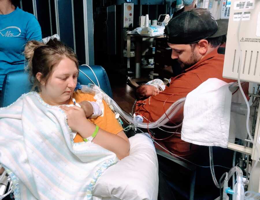 Couple look forlorn while holding their NICU preemie twins while hooked up to tubes and monitors