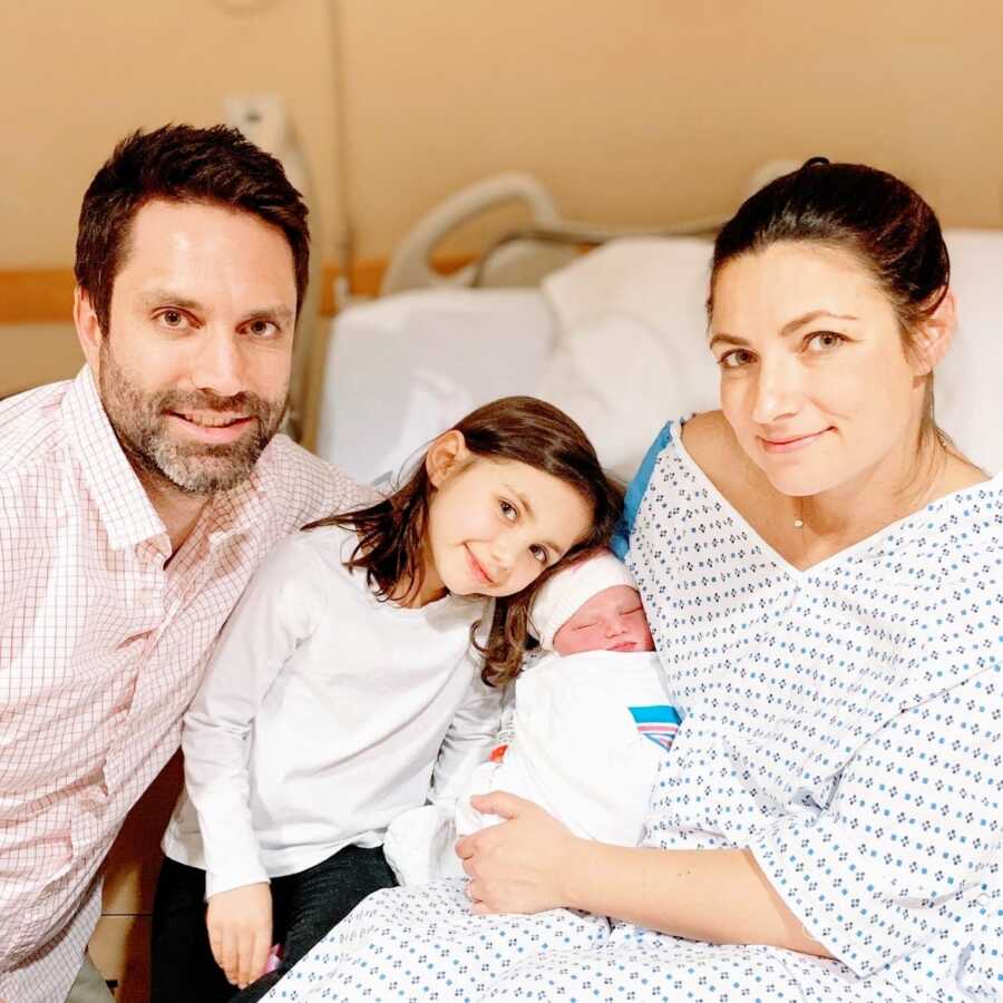 Family of four take a photo together in the hospital with their newborn baby daughter