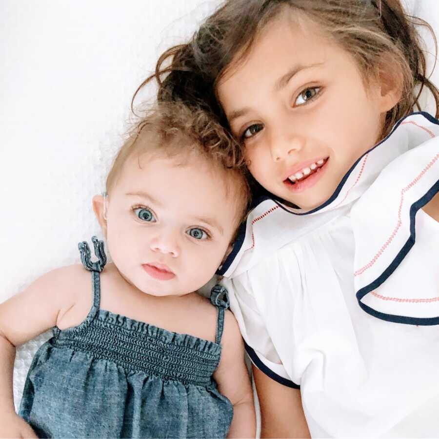 Two sisters spend some bonding time together, one in a white dress and one in a blue denim dress