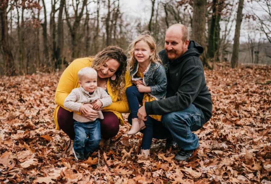 Family of four take fall-themed photos together while standing in brown leaves outside