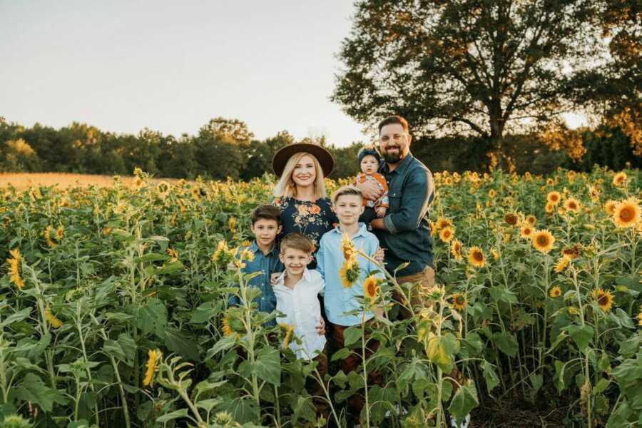 Family of six take photos together in a field of sunflowers during the sunset