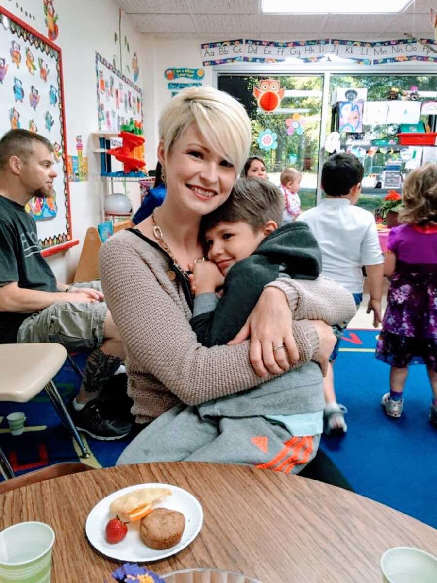 Mom of three snuggles one of her sons while at a school function in his classroom