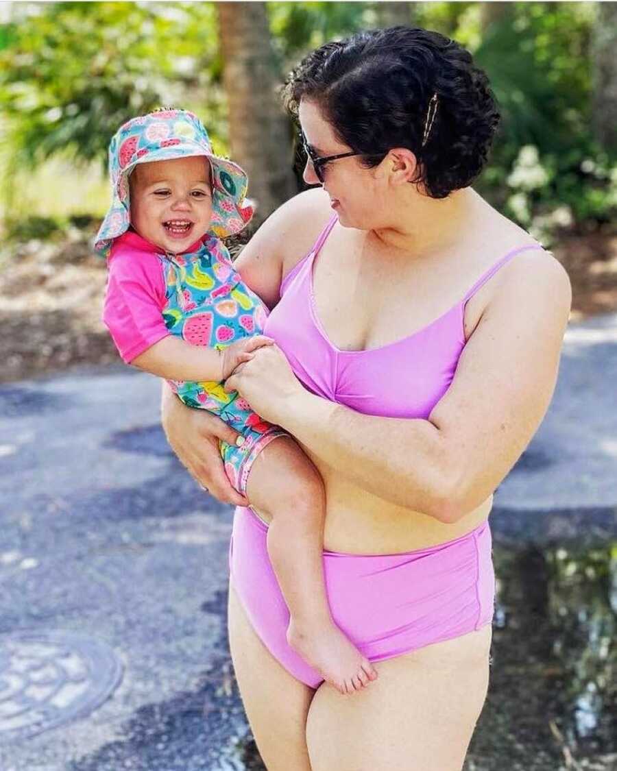 Single adoptive mom holds one of her daughters while smiling at her, both in bathing suits