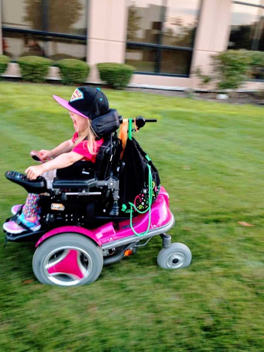 Little girl with cerebral palsy squeals in delight as she zooms by her mom in her hot pink motorized wheelchair