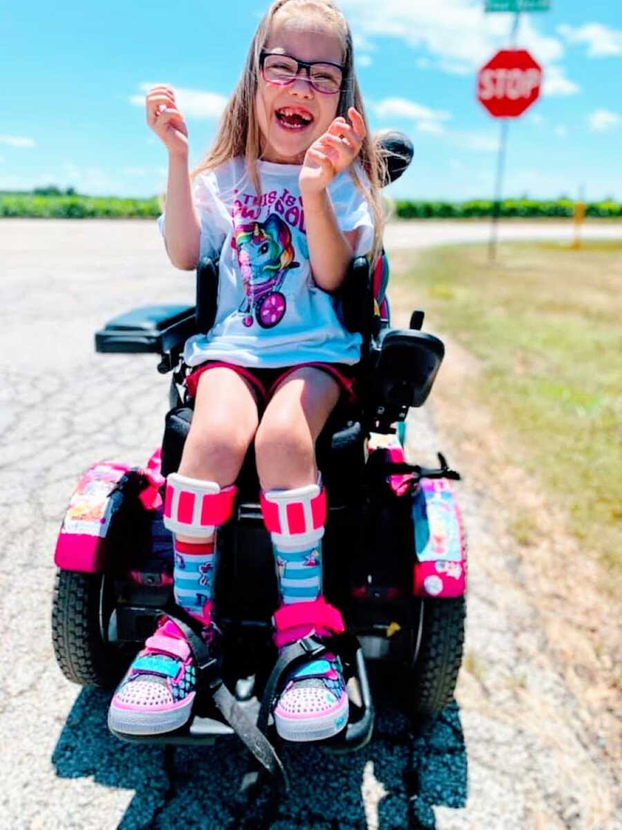 Little girl with cerebral palsy smiles big in her wheelchair during a family outing