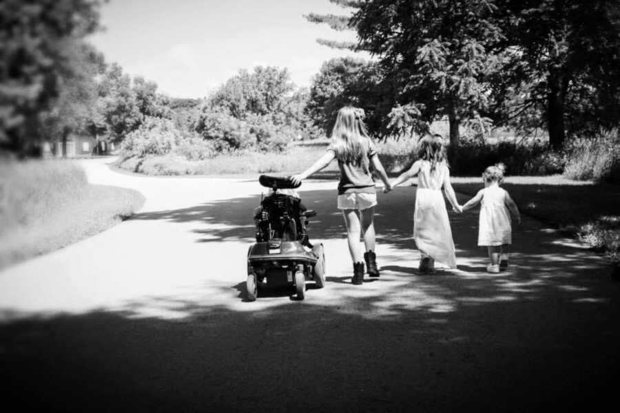 Mom of four girls takes a photo of her daughters walking down the street hand in hand, while one rides in her wheelchair