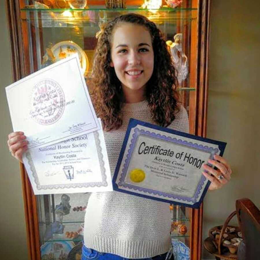 Young teen girl in high school poses with the several honors and awards she won