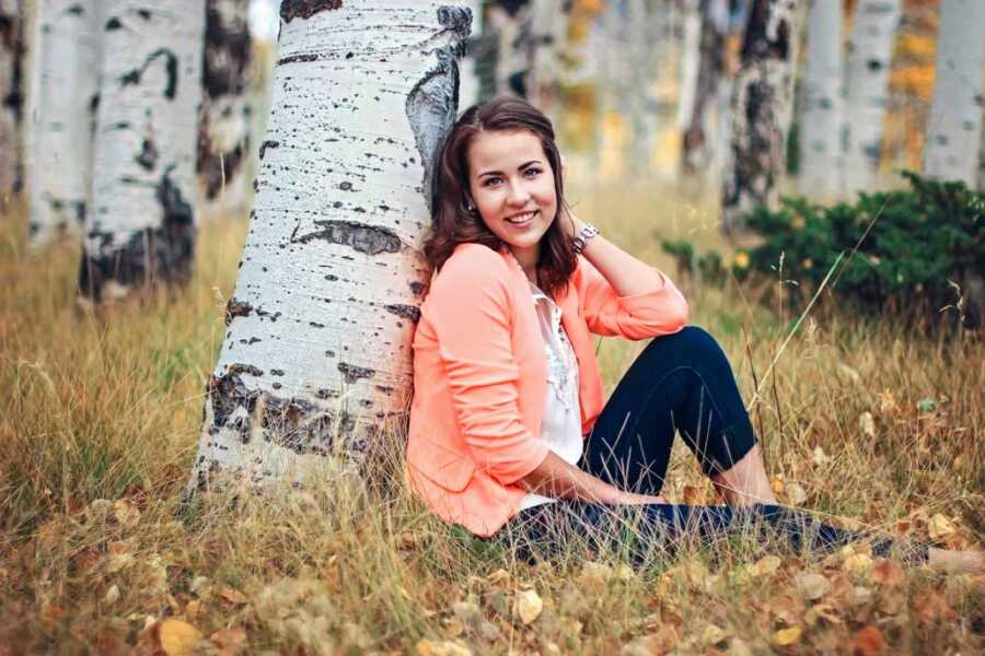 Birth mother sits against a tree trunk while taking professional photos