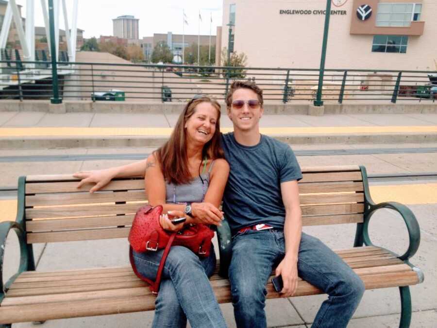 Young man sits with his birth mother on a bench outside while spending time together and getting to know one another