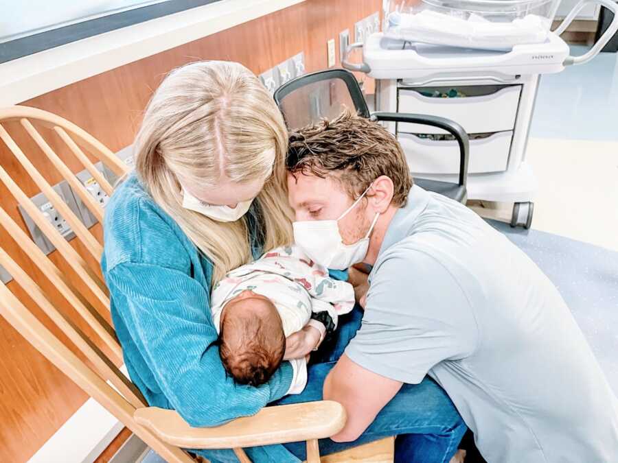 Young couple hold a newborn baby in the hospital, staring in awe as he sleeps